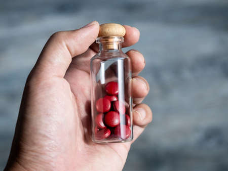 Close up red vitamins or supplements in the small clear glass bottle vials in person's hand. Hand...
