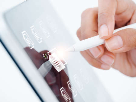 Document management. Cloud computing technology. Closeup document file information icons and check mark on tablet computer screen, choosing by digital pencil in hand, online digital databases concept.の写真素材