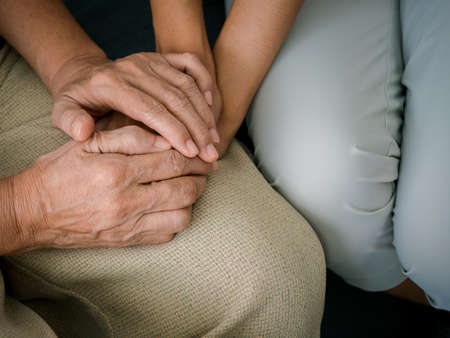 Close up of old mother, grandmother, elder or senior woman's hands hold her daughter or grandchild's hands for support with care and comfort. Giving love and encouragement concept.の写真素材
