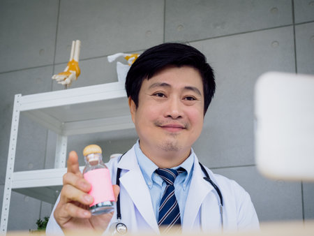 Portrait of Asian male doctor in white uniform with a stethoscope explaining about medicine in bottle, drug use, online video call and consulting patient. Healthcare medical and Telemedicine concept.の写真素材