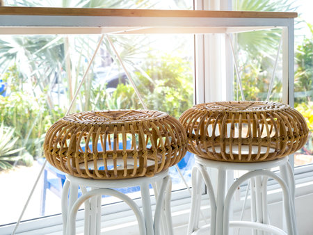 Two empty round rattan bar stool chairs near the table and glass window decoration in cafe with green tropical palm tree view outside.の写真素材