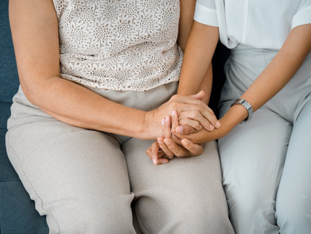 Close up of old mother, grandmother, elder or senior woman's hands hold her daughter or grandchild's hands for support with care and comfort. Giving love and encouragement concept.の写真素材
