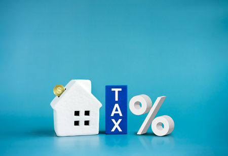 Home tax concept, residential, real estate property, land, building annual taxation. Word, Tax on blue blocks and coins fall in white small house, percentage icon on blue background with copy space.の写真素材