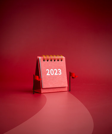 2023 year small red desk calendar standing between finish flags on road to success on red...