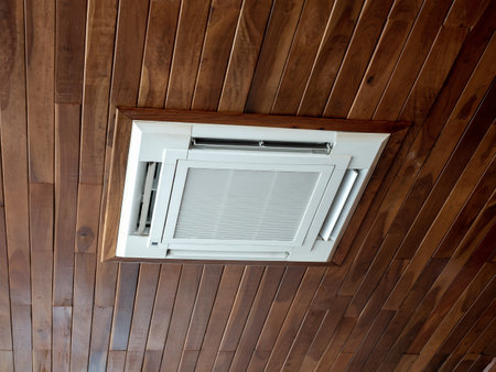 Ceiling mounted cassette type air conditioner system on wooden ceiling. White ceiling air conditioning decoration on wood plank background.の写真素材