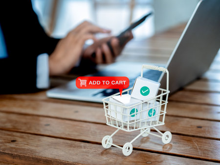 Add to cart icon sign appear on white shopping trolley cart contained parcel boxes with check marks near the business person who using smart mobile phone and laptop computer, online shopping concept.の写真素材
