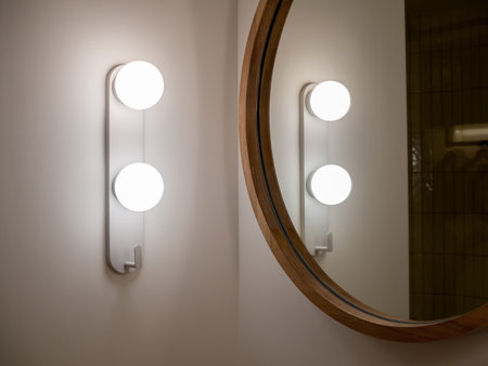 Modern mounted wall light lamp near the round shape wooden mirror on white wall background in the bathroom. Lighting, ball shape decoration on the corner of the bathroom wall in the hotel.の写真素材
