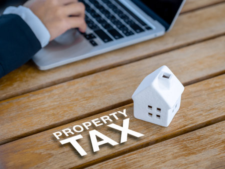 Home tax, refinance, house mortgage, loan, investment housing real estate interest rates concepts. The 3d word "PROPERTY TAX" and miniature house on desk near business person using laptop computer.の写真素材