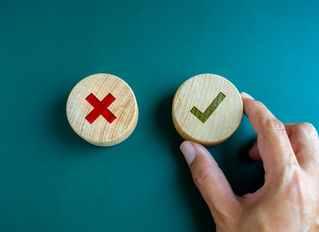 Right and wrong. Close-up green check mark and red X mark icon on round wooden button, chosen green check mark by business's hand. Picking correct sign. Approving, voting or right decision concepts.の写真素材