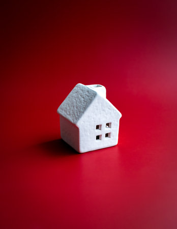 Home, house, family, real estate, property and residential concepts. White minimal miniature ceramic small house standing alone isolated on red background, vertical style.の写真素材