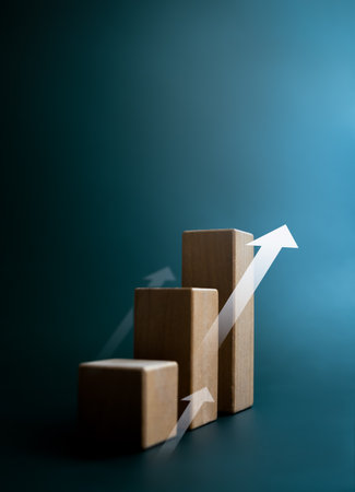 Rise up arrow on wooden cube blocks, bar graph chart steps on dark blue background with copy space, vertical style. Investment, income, inflation, business growth, economic improvement concepts.の写真素材