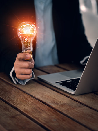Business solution, learning and creative idea management concepts. Glowing brain symbol and cogs, management icon system inside light bulb, hold by business people who work with computer, vertical.の写真素材
