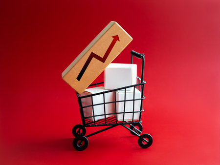 Inflation, increase sales, high price, rising cost of shopping, business marketing concepts. Growth arrows on wood block and white parcel boxes in black shopping cart trolley on red background.の写真素材