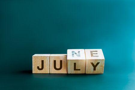 Changing the month of mid of the year. Flipping wooden cube blocks for change words, months from June to July, isolated on blue background with copy space, clean, modern, and minimal style.の写真素材