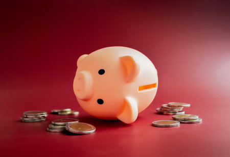 The empty pink piggy bank fall down around with little pile of less money coins on red background. Inflation, low cost, crisis economic, personal saving rate, low savings ratio concepts.の写真素材