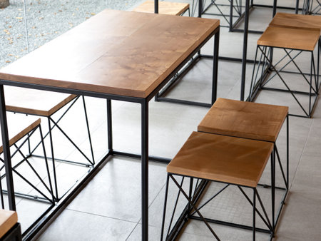 Empty wood of wooden table set with chairs on cement tiles background with no people, loft style cafe interior. Empty wood furniture with black steel bar decoration on concrete  ground floor in cafe.の写真素材