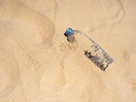Plastic bottle on sandy beach, top view. Empty uncapped used plastic drinking water bottles piled up with sand, dumped on the beach with copy space. Polluted garbage abandoned by tourists.の写真素材