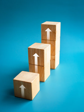 Rising up arrows shining on wooden cube blocks bar graph chart steps on blue vertical background, minimal style. Purchase trend increase, income, inflation, business marketing growth concepts.の写真素材