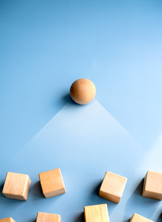 Wooden sphere stand alone at the leader position of group of wood cube blocks on blue background,...