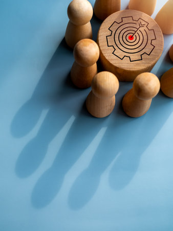 Target icon on round wood block surrounded with small wooden human figures made a crown shape shadow...
