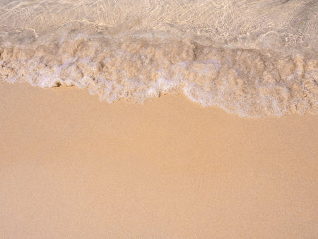 Bright beach background, movement of clear sea water and wave surf on clean sandy beach ocean, seashore scene, coastline. Top view beach with copy space, summer vacation holiday poster background.の写真素材