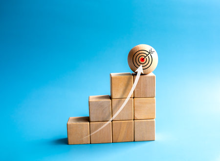 Rise up arrows shoot up towards the goal. Target icon on wooden sphere, top of wood cube block bar graph chart steps on blue background. Business growth process, trend, economic improvement concepts.の写真素材