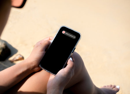 Slide to power off option on mobile smart phone display screen  stylish female's hands who wearing sunglasses, relaxsit with cross legs on sandy beach at the sea front, summer vacation, holiday trip.の写真素材