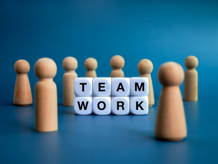 Teamwork, team, leadership and family business concepts. Words "TEAMWORK", text on white cube blocks and different wooden people figures standing in front of the big target icon on blue background.の写真素材