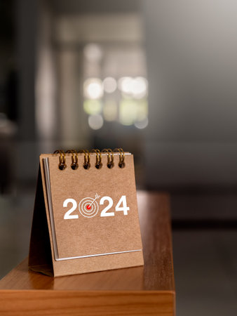Happy new year 2024 banner background. 2024 numbers year with target icon on brown small desk calendar cover standing on table edge in office, vertical style. Business goals and success concepts.の写真素材
