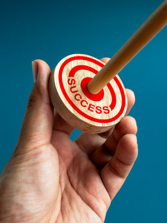 Target and business goal concepts. Word "SUCCESS" and big red target dart icon on round wooden was hit by wood arrow on center position, hold by businessman's  hand on blue background, vertical style.の写真素材