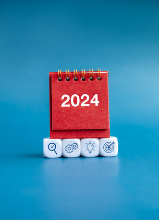 Happy new year 2024 banner background concept. Business strategy plan icons on white blocks and 2024 numbers year on red small desk calendar cover standing isolated on blue background, vertical style.の写真素材