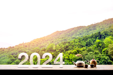 Happy ne year 2024 concept with letter numbers and Asian style hot tea set on wooden table on green mountain view with sunrise in the morning at Chiang Mai, the famous province north of Thailand.の写真素材