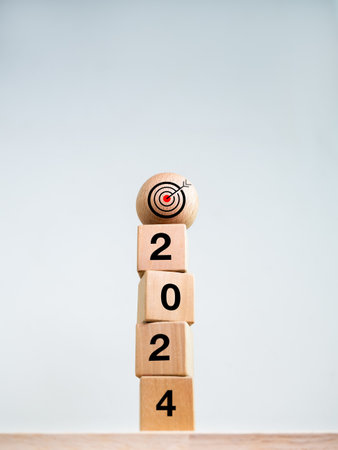 2024 Happy New year background. Target icon on wood sphere on top of 2024 year numbers on wooden cube blocks stack on white background, vertical style. Welcome, Merry Christmas. Business goal concept.の写真素材