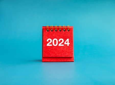 Happy new year 2024 banner background. 2024 white numbers year on red small desk calendar cover standing on light blue background, minimal style. Business goals plan and success schedule concepts.の写真素材