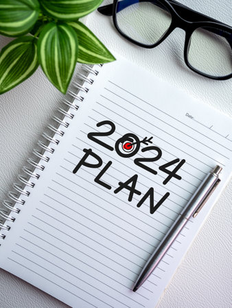 Goals, action and plan, resolution concept in new year 2024. Handwriting text, 2024 PLAN with target dart icon with pen on white notebook page, top view near green leaves and glasses, vertical style.の写真素材