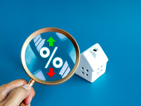 Home tax concept. Real estate, land and property annual taxation. Percentage icon with green up and red down arrow and white house model in magnifying glass lens, hold by hand, on blue background.の写真素材