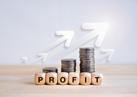 Business growth, revenue, investment, income, savings and balance concept. Text "PROFIT" on wooden cube blocks with money coin stacks graph steps with rising arrows on wood table and white background.の写真素材