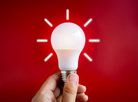 Glowing white light bulb with graphic radius neon style, holding by hand isolated on dark red...