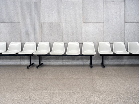 Scene of row of empty waiting chair set with white plastic seats with black iron legs seats on grey tiles and concrete wall background inside the modern building with no people.の写真素材