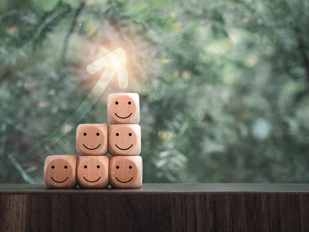 Rising up arrow on wooden cube blocks as a business graph or chart steps with happy smile faces on table and green leaves background with copy space. Business growth, satisfaction, rating concepts.の写真素材