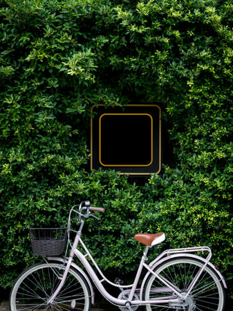 Square black blank shop sign surrounded with green bush with vintage bicycle, vertical style. Mockup yellow frame sign board at restaurant, shop or cafe, mounted on leaves wall. signage template.の写真素材