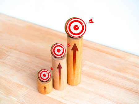 3d Target icons and rise arrows on round wooden sticks as business graph steps on wood desk on white background. Business growth graph process, goal, success, and economic improvement concepts.の写真素材