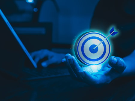 Businessman hand holding big goal, target dart icon while working with laptop computer, blue tone. Business strategy, action plan and future innovation technology with goal and success concepts.の写真素材