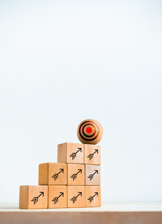 Big target icon on wooden sphere on top of cube blocks bar graph chart steps with arrows symbol on desk, white vertical background. Investment, income, revenue, profit goal, business growth concepts.の写真素材
