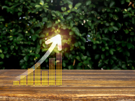 Rise up glowing arrow on virtual digital business chart graph steps on table and green leaves background with copy space. Business growth, investment, sustainable development goals concepts.の写真素材