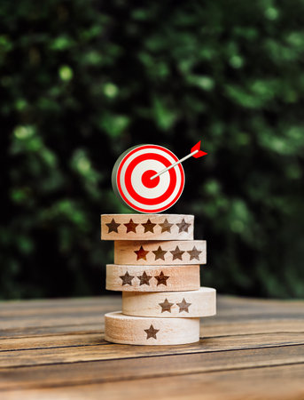 3d goal target icon on top of round wood block stack with one to five stars rating symbols, on green leaves background, vertical style. Business marketing, evaluation, rating, customer review concept.の写真素材