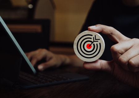 Businessman hand holding big goal, target dart icon on circle wooden while working with laptop computer. Business strategy, action plan and future innovation technology with goal and success concepts.の写真素材