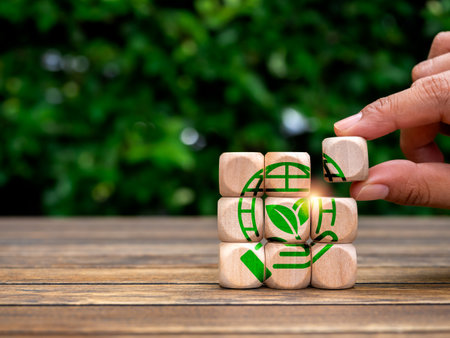 Earth care, global warming, environment responsibility, world earth day concepts. Green hand hold world, symbol in hand put on wooden cube puzzle blocks on green leaves background with copy space.の写真素材