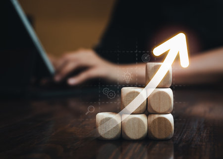 Arrow rising on wooden cube blocks as graph steps with strategy icons while businessperson working with laptop computer. Business market growth, goal and success, progress and management concepts.の写真素材