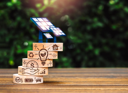 Sustainability eco, earth care, saving power and energy concept. Solar panels being installed on wooden cube stack with ecology system icons, on wood table and green leaves background with copy space.の写真素材